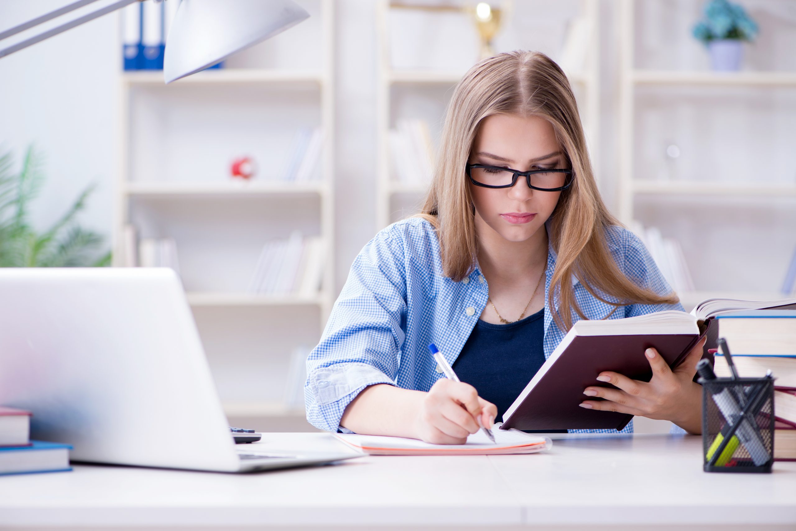 Teenager revising with book and laptop, writing notes